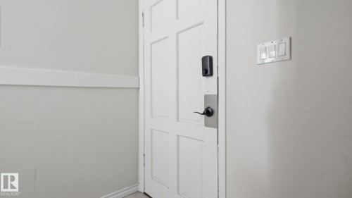 White paneled interior door with black hardware, electronic lock, and adjacent wall-mounted light switches - 12208 146 Avenue Nw, Edmonton, AB 