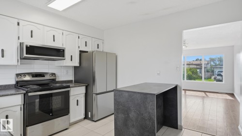 Kitchen featuring white cabinetry, stainless steel appliances, a black countertop, and a built-in island - 12208 146 Avenue Nw, Edmonton, AB 