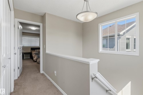 Carpeted hallway with a window featuring white trim, a semi-flush mount ceiling light, and a white railing - 1608 65 Street Sw, Edmonton, AB - Indoor Photo Showing Other Room