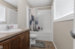 Bathroom featuring a white tub-shower combination, a vanity with wood-finish cabinetry, a white rectangular sink, and chrome fixtures - 