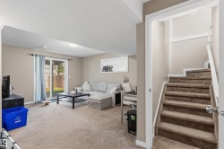 Carpeted staircase leading to a spacious lower-level room featuring light tan walls and recessed lighting - 