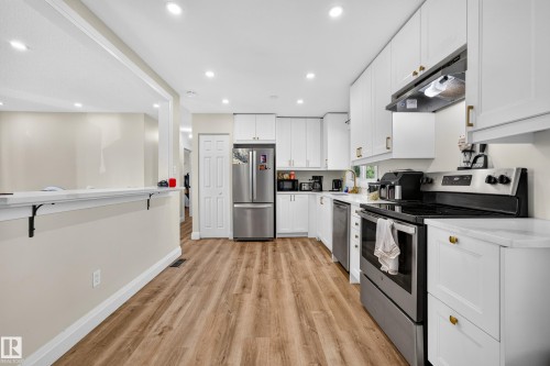 Kitchen featuring wood-finish flooring, white cabinetry, stainless steel appliances, and recessed lighting - 2412 80 Street Nw, Edmonton, AB 