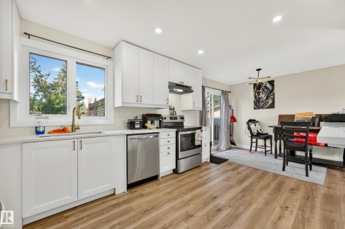 Kitchen featuring white cabinetry, wood-finish flooring, stainless steel appliances, and a sliding glass door - 2412 80 Street Nw, Edmonton, AB 