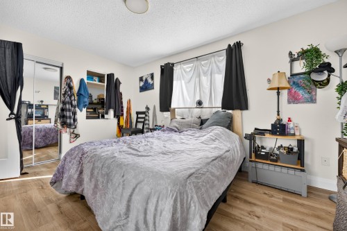 Wood-finish flooring, mirrored sliding closet doors, built-in wall shelving, and window with dark curtain panels - 2412 80 Street Nw, Edmonton, AB 