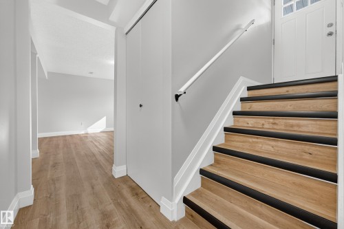 Wood-finish stairs with black tread accents and a white handrail - 2412 80 Street Nw, Edmonton, AB 