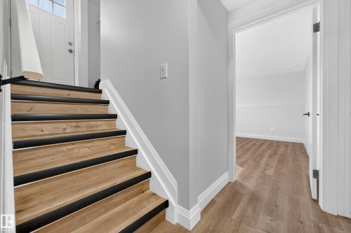Wood-finish staircase with black treads and white risers, complementing light wood-finish flooring - 2412 80 Street Nw, Edmonton, AB 
