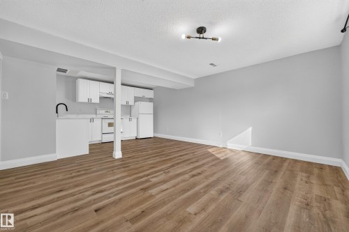 Open-concept living area featuring wood-finish flooring, white cabinetry, integrated appliances, a matte black gooseneck faucet, and contemporary ceiling lighting - 2412 80 Street Nw, Edmonton, AB 