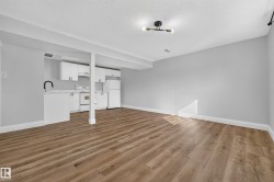 Open-concept living area featuring wood-finish flooring, white cabinetry, integrated appliances, a matte black gooseneck faucet, and contemporary ceiling lighting - 