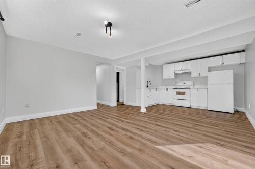 Open-concept living space featuring wood-finish flooring, a full kitchen with white cabinetry, a complete set of appliances, and track lighting - 2412 80 Street Nw, Edmonton, AB 