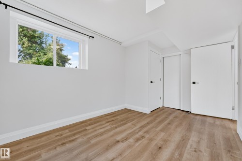 Room featuring wood-finish flooring, a white-framed window, and white interior doors with black hardware - 2412 80 Street Nw, Edmonton, AB 