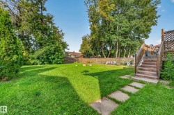 Expansive backyard featuring a lush lawn, mature trees, a wood-slat fence, and concrete stepping stones - 