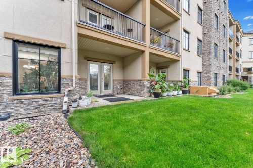 Ground-level patio with double glass doors, surrounded by stacked stone and stucco exterior - #105 160 Magrath Rd Nw, Edmonton, AB 