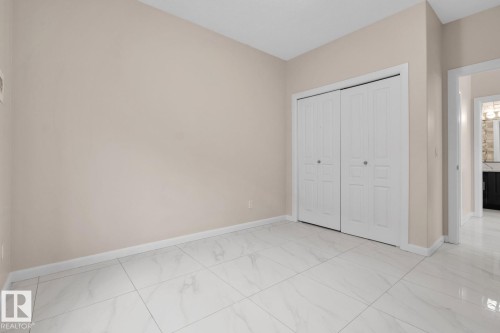 White tile flooring, neutral wall paint, and white bi-fold closet doors - #105 160 Magrath Rd Nw, Edmonton, AB 
