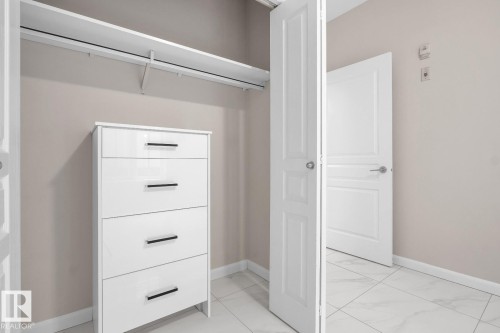 Walk-in closet with white shelving and a hanging rod, complemented by neutral wall tones - #105 160 Magrath Rd Nw, Edmonton, AB 