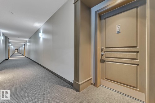 Building corridor with wall sconces, carpeted flooring, and paneled entry door - #105 160 Magrath Rd Nw, Edmonton, AB 
