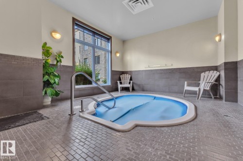 Indoor spa with a tiled surround, stainless steel grab rail, and large windows - #105 160 Magrath Rd Nw, Edmonton, AB 