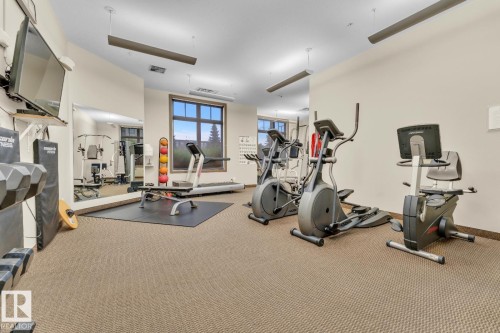 Carpeted fitness area with wall-mounted mirror, large window, and recessed lighting - #105 160 Magrath Rd Nw, Edmonton, AB 