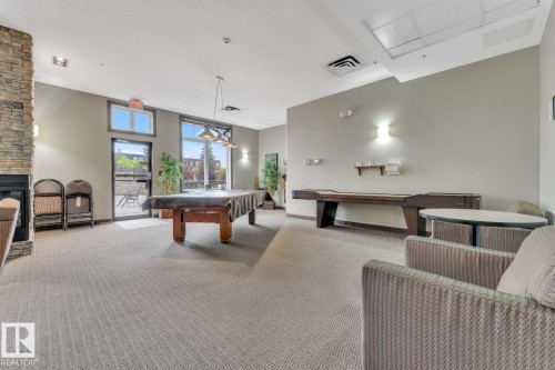 Stone-clad fireplace with a built-in firebox, large windows, glass-paneled exterior door, and recessed ceiling lighting - #105 160 Magrath Rd Nw, Edmonton, AB 