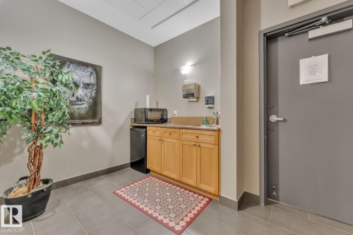 Compact kitchenette with wood cabinetry, light-toned countertop, and tile flooring - #105 160 Magrath Rd Nw, Edmonton, AB 