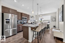 Kitchen featuring wood-finish flooring, stainless steel appliances, dark wood cabinetry, a tiled backsplash, and a breakfast bar with pendant lighting - 
