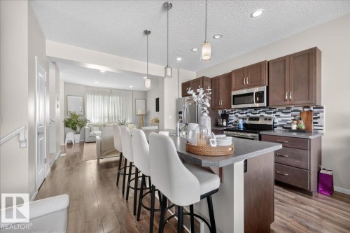 Expansive kitchen with wood-finish flooring, dark wood cabinetry, stainless steel appliances, and a tiled backsplash - 2046 Chalmers Way Sw, Edmonton, AB 