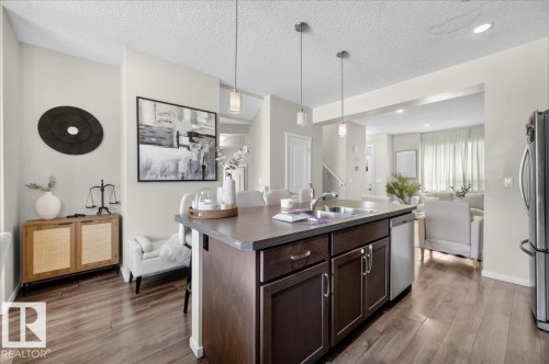Kitchen island with integrated sink, dark wood-finish cabinetry, and stainless steel dishwasher - 2046 Chalmers Way Sw, Edmonton, AB 