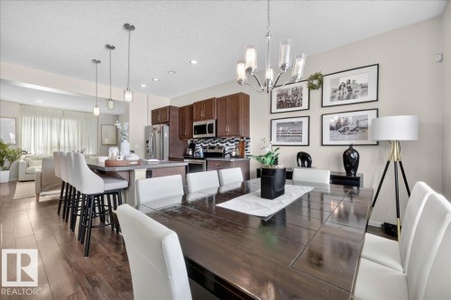 Open-concept living space with wood-finish flooring, a kitchen island, pendant lighting, and a chandelier - 2046 Chalmers Way Sw, Edmonton, AB 