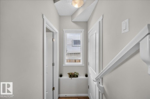 Hallway with wood-finish flooring, white trim, and a window with blinds - 2046 Chalmers Way Sw, Edmonton, AB 