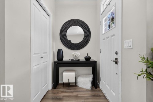 Entryway featuring wood-finish flooring, a white paneled door with glass inserts, and a built-in closet with bi-fold doors - 2046 Chalmers Way Sw, Edmonton, AB 