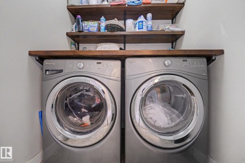 Integrated laundry area featuring two front-loading machines, a wood-finish countertop, and two open wood-finish shelves - 3343 Weidle Way Sw, Edmonton, AB 