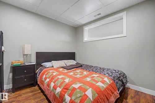 Bedroom featuring wood-finish flooring, light gray walls, a white drop ceiling, and a high horizontal window - 3343 Weidle Way Sw, Edmonton, AB 