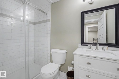 Bathroom featuring a glass-enclosed shower with subway tile surround, a single vanity with a white countertop, and a framed mirror - 3343 Weidle Way Sw, Edmonton, AB 