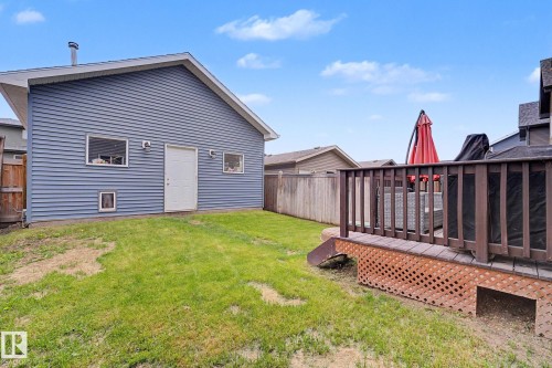 Expansive backyard featuring a manicured lawn, a two-story residence with blue siding, and a raised wood deck with lattice skirting - 3343 Weidle Way Sw, Edmonton, AB 
