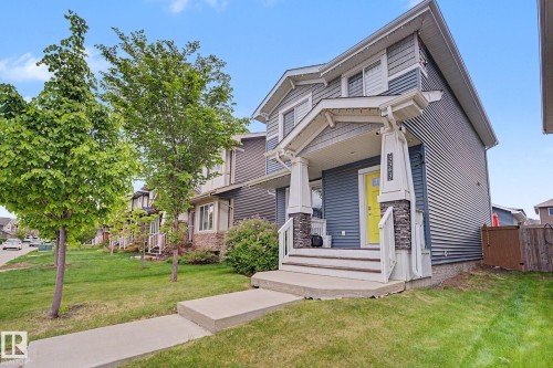 Two-story residence featuring a covered front porch with stone-clad pillars, a bright yellow entry door, and horizontal siding - 3343 Weidle Way Sw, Edmonton, AB 