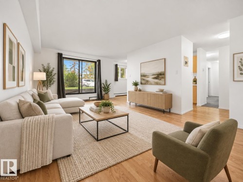 Spacious living area featuring wood-finish flooring, white walls, and a large window - #119 3611 145 Av Nw, Edmonton, AB 