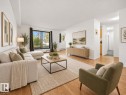 Spacious living area featuring wood-finish flooring, white walls, and a large window - #119 3611 145 Av Nw, Edmonton, AB 