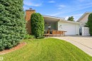 Brick chimney, wood-finish ramp, attached garage with white door, concrete driveway, and mature landscaping - 9311 68 Street Nw, Edmonton, AB 