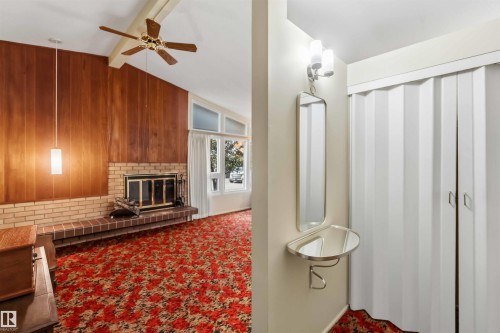 Vaulted ceiling with an exposed beam, a brick fireplace with a raised hearth, wood paneling, and an accordion-style closet door - 9311 68 Street Nw, Edmonton, AB 