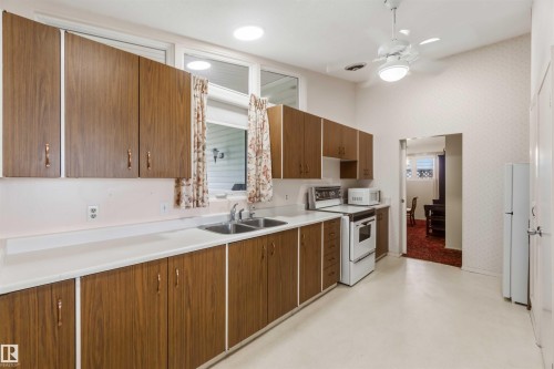 Galley kitchen featuring wood-finish cabinetry, white countertops, a double basin sink, and a white ceiling fan - 9311 68 Street Nw, Edmonton, AB 