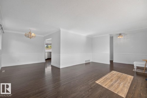 Dark wood-finish flooring, white crown molding, wall paneling, and a chandelier with a central light fixture - 7304 98A Avenue Nw, Edmonton, AB 