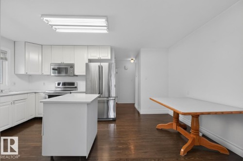 Kitchen featuring white cabinetry, stainless steel appliances, a center island with a white countertop, and dark wood-finish flooring - 7304 98A Avenue Nw, Edmonton, AB 
