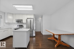 Kitchen featuring white cabinetry, stainless steel appliances, a center island with a white countertop, and dark wood-finish flooring - 