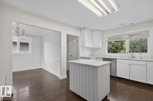 Kitchen featuring white cabinetry, a central island, a stainless steel dishwasher, and a window with natural scenery - 7304 98A Avenue Nw, Edmonton, AB 