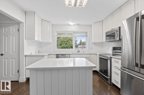 White cabinetry, stainless steel appliances, white countertops, wood-finish flooring, and a central island with beadboard paneling - 7304 98A Avenue Nw, Edmonton, AB 