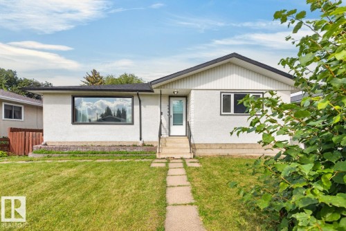 Front exterior with a white stucco finish, a black-framed picture window, and a gray shingled roof - 7304 98A Avenue Nw, Edmonton, AB 