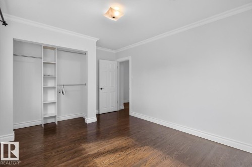 Hardwood flooring, recessed closet with built-in shelving and hanging rods, white interior door with black hardware, crown molding, and a flush-mount ceiling light - 7304 98A Avenue Nw, Edmonton, AB 