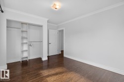 Hardwood flooring, recessed closet with built-in shelving and hanging rods, white interior door with black hardware, crown molding, and a flush-mount ceiling light - 