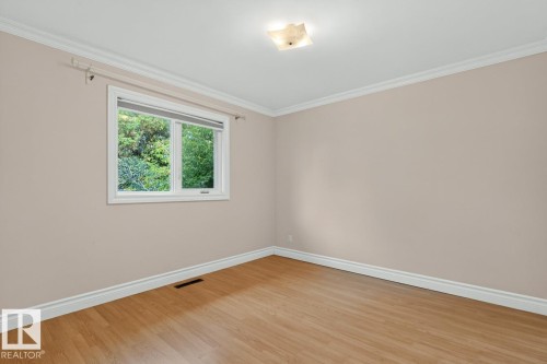 Wood-finish flooring, white crown molding, white baseboards, and a flush mount ceiling light fixture - 7304 98A Avenue Nw, Edmonton, AB 