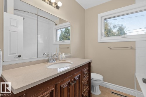 Bathroom featuring a wood-finish vanity with a light-toned countertop, undermount sink, and chrome fixtures - 7304 98A Avenue Nw, Edmonton, AB 