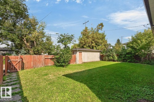 Expansive green lawn with mature trees, a wood privacy fence, and an auxiliary building - 7304 98A Avenue Nw, Edmonton, AB 